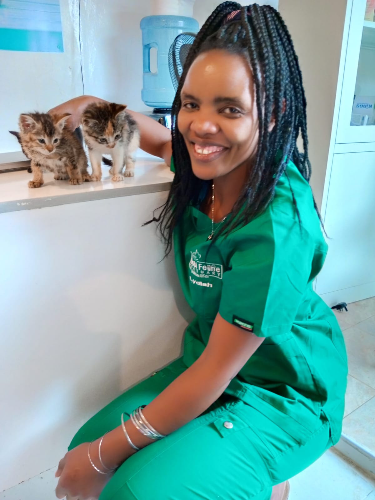 Nairobi Feline Sanctuary staff member in green scrubs beside two kittens.